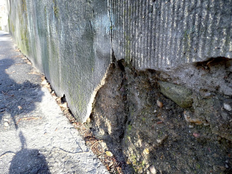 Uszkodzenia tynku czesanego oraz znaczne ubytki w podłożu betonowym.